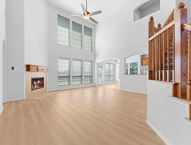 8401 Hitching Trail McKinney, TX 75070 - Photo 27 of 39 Unfurnished living room with arched walkways, a high ceiling, a ceiling fan, light wood-type flooring, and a tiled fireplace