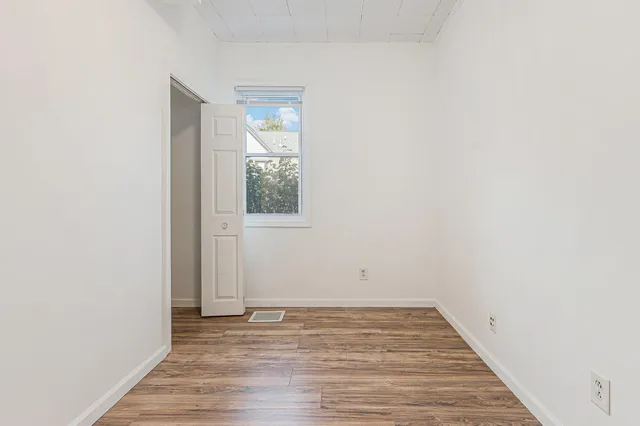 a view of an empty room with wooden floor and a window
