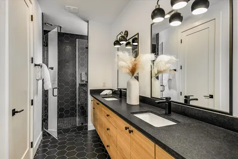 a bathroom with a granite countertop double vanity sink a mirror and shower
