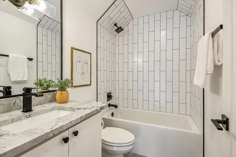 a bathroom with a granite countertop bathtub sink vanity mirror and toilet