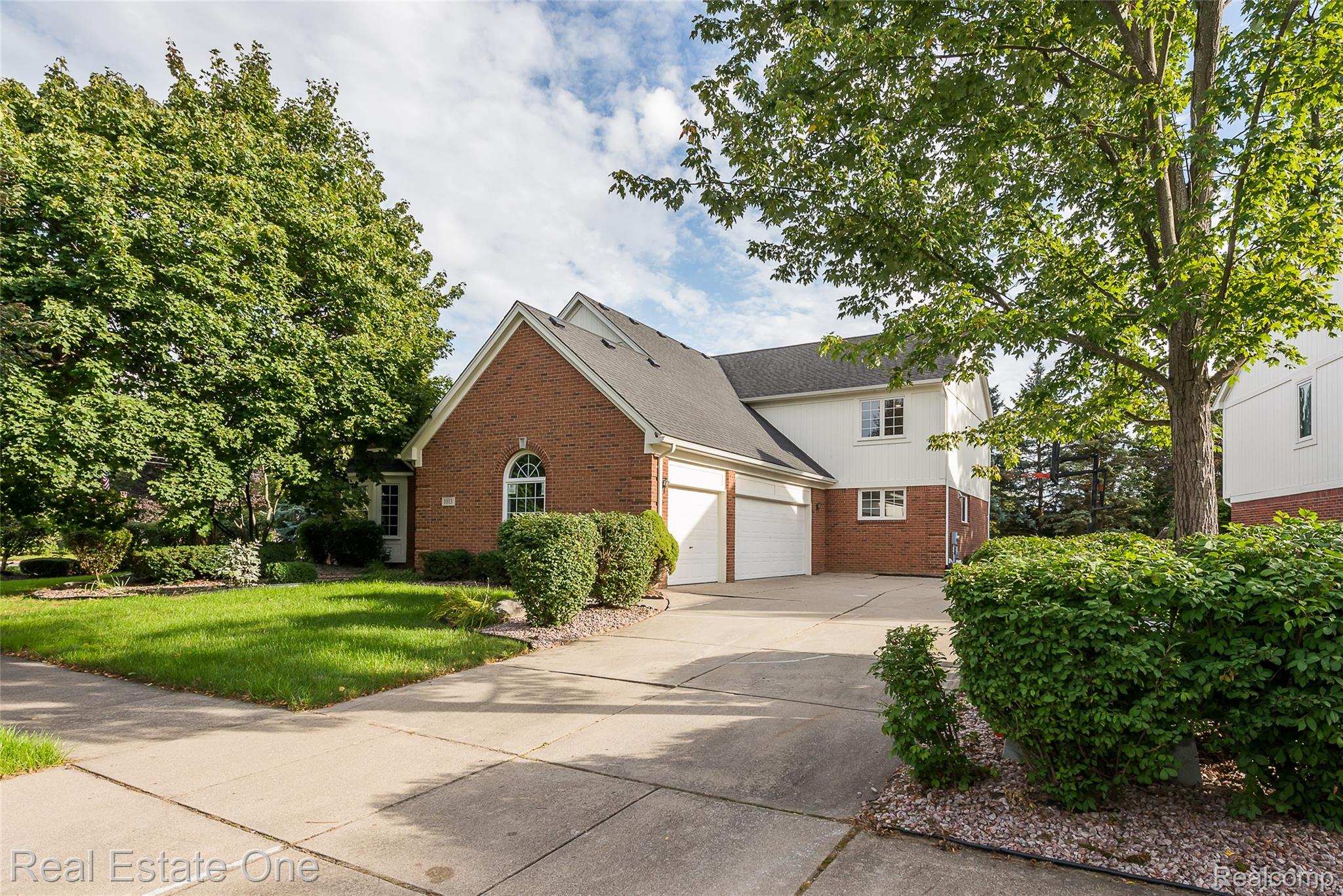 1013 Rochelle Park Drive Rochester, MI 48307 - Photo 61 of 74 Brick and siding exterior featuring an arched window, two garage doors, and mature trees