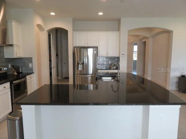 a kitchen with stainless steel appliances kitchen island granite countertop a refrigerator a stove and a sink with wooden floor