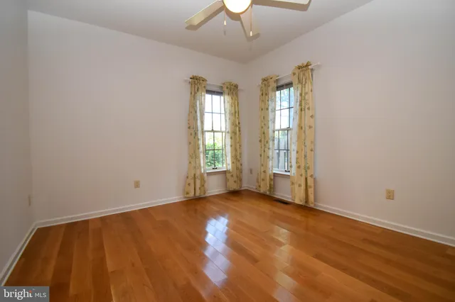an empty room with wooden floor chandelier fan and windows