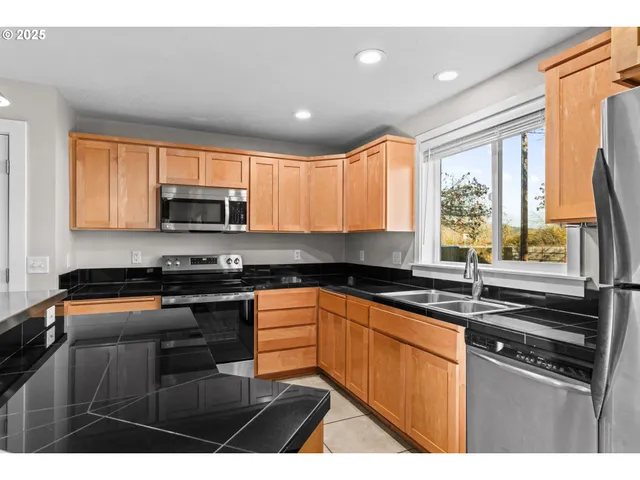 a kitchen with stainless steel appliances a sink a stove a microwave a refrigerator cabinets and a window
