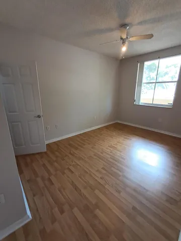 an empty room with wooden floor fan and windows