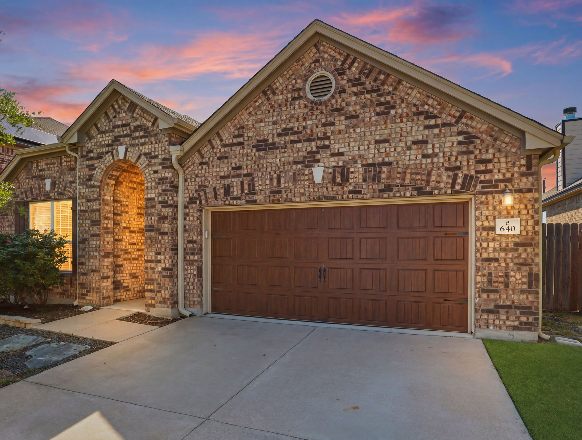 640 Landon Samuel Loop Pflugerville, TX 78660 - Photo 2 of 33 Brick exterior featuring an arched entry, a two-car garage with a wood-finish door, and concrete driveway