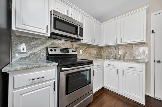 a kitchen with granite countertop white cabinets stainless steel appliances and a wooden floor