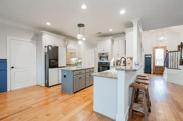 a large kitchen with stainless steel appliances kitchen island a stove a refrigerator a sink dishwasher a oven with white cabinets and wooden floor