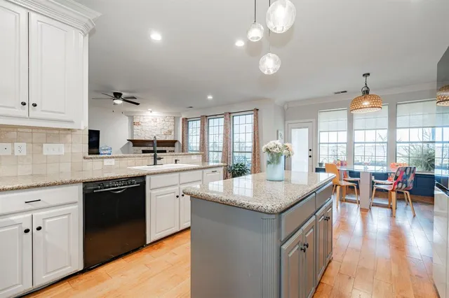 a open kitchen with granite countertop a sink dishwasher stove and white cabinets with wooden floor