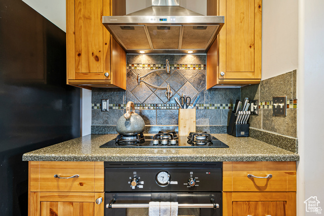 2029 West Tollgate Road Coalville, UT 84017 - Photo 14 of 43 Kitchen with black appliances, wall chimney range hood, tasteful backsplash, brown cabinetry, and dark stone counters