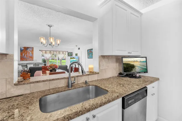 a kitchen with granite countertop a sink a counter top space cabinets and stainless steel appliances