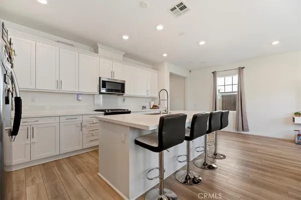 a kitchen with stainless steel appliances granite countertop a stove a sink a refrigerator white cabinets and wooden floor