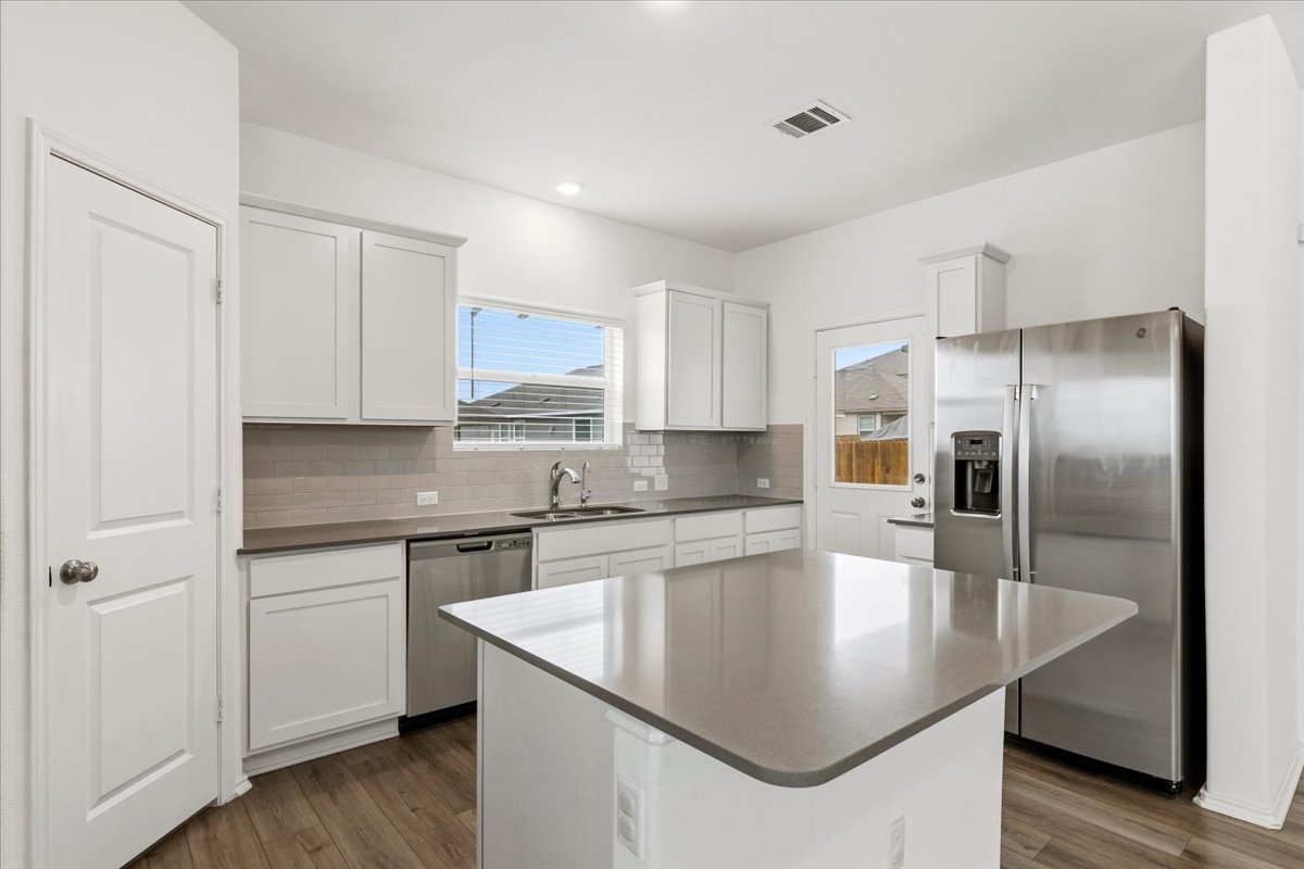 101 Rowdy Yates Way Jarrell, TX 76537 - Photo 8 of 32 Kitchen featuring a central island with a solid surface countertop, white cabinetry, stainless steel appliances, a subway tile backsplash, and wood-finish flooring