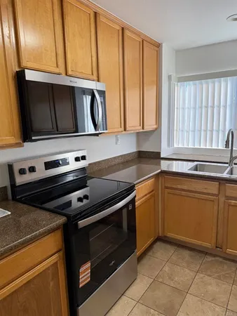 a kitchen with granite countertop a refrigerator a stove and a sink with wooden cabinets