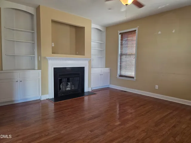 a view of an empty room with wooden floor fireplace and a window