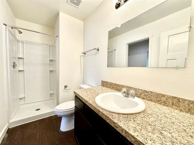 a bathroom with a granite countertop sink a toilet a mirror and shower