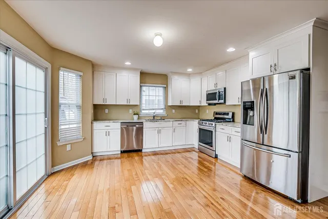 a kitchen with granite countertop a refrigerator oven a sink dishwasher and white cabinets with wooden floor