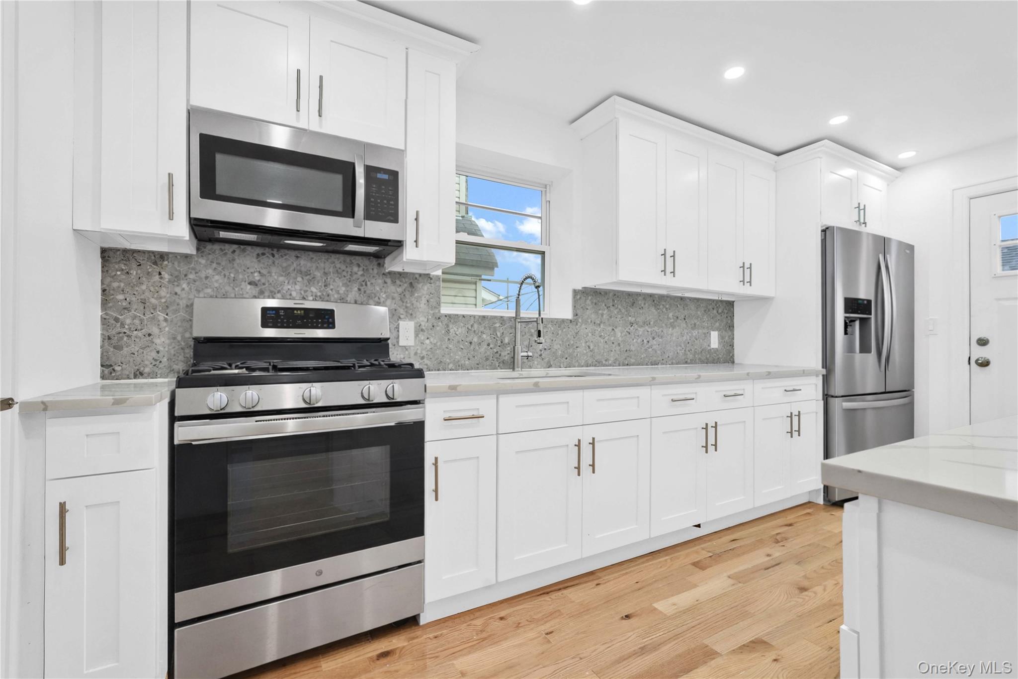 21432 112th Road Queens, NY 11429 - Photo 11 of 18 Kitchen featuring stainless steel appliances, white cabinetry, light wood finished floors, light stone counters, and recessed lighting
