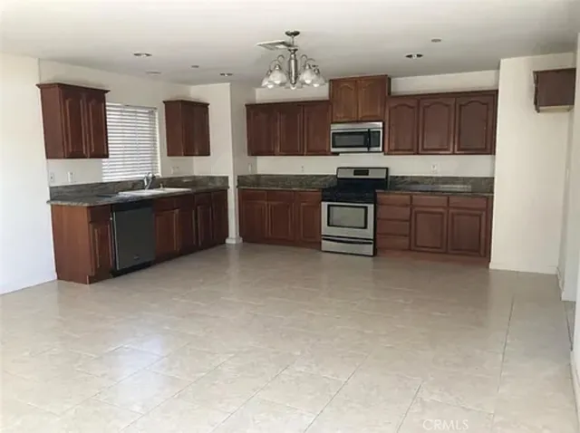 a kitchen with stainless steel appliances granite countertop a stove top oven a sink dishwasher and a refrigerator with wooden cabinets