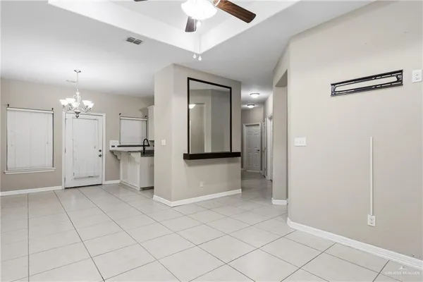 an empty room with kitchen view and a chandelier fan