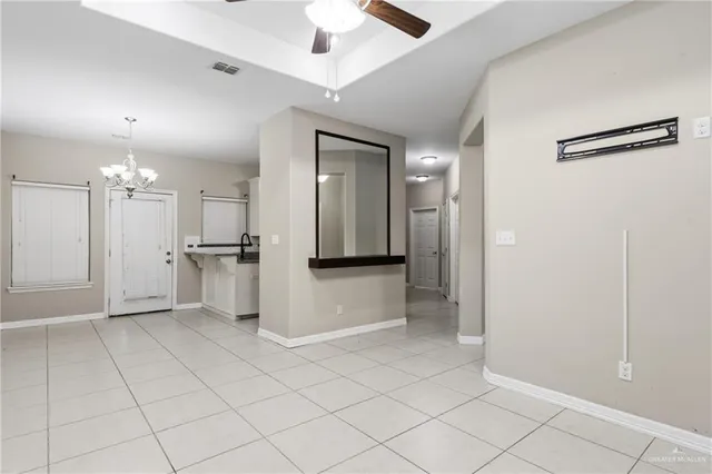 an empty room with kitchen view and a chandelier fan