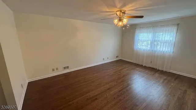 an empty room with wooden floor chandelier fan and windows