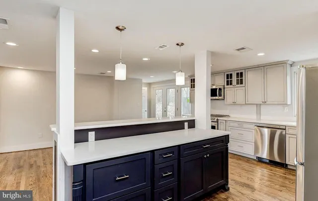 a large white kitchen with stainless steel appliances kitchen island granite countertop a stove a sink a refrigerator and white cabinets with wooden floor