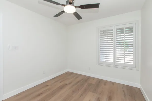 an empty room with wooden floor fan and windows