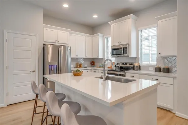 a kitchen with stainless steel appliances granite countertop a refrigerator a sink a stove a dining table and chairs