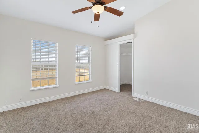 an empty room with chandelier fan and windows