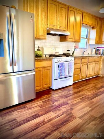 a kitchen with stainless steel appliances granite countertop a refrigerator a sink dishwasher a stove and white cabinets with wooden floor