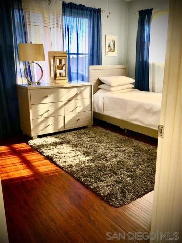 a bedroom with a bed and dresser with wooden floor