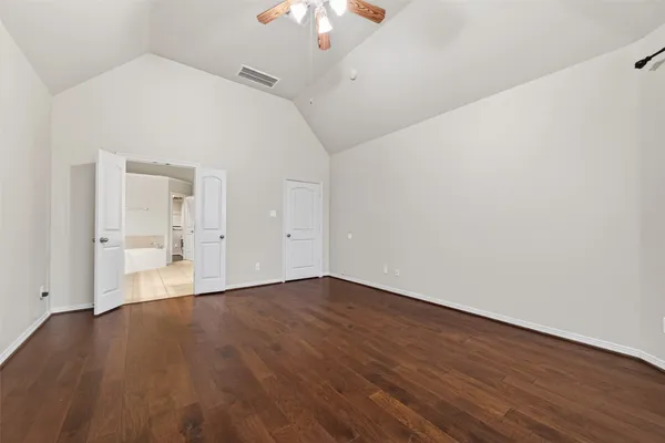 a view of an empty room with wooden floor and a ceiling fan