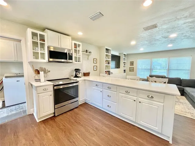 a kitchen with stainless steel appliances white cabinets a sink a stove a microwave and wooden floors