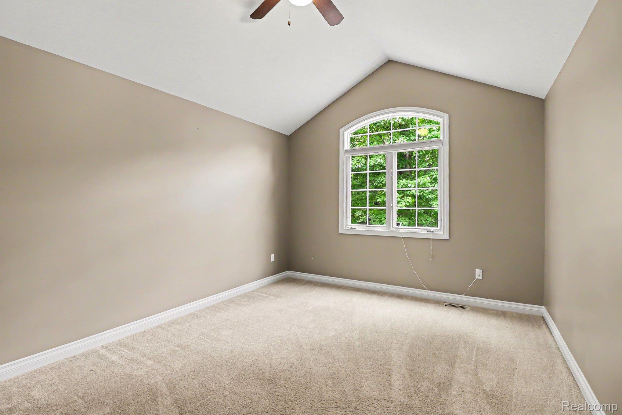 10490 Deer Ridge Trail Holly, MI 48442 - Photo 28 of 56 Arched window with multiple panes, vaulted ceiling, neutral wall color, tan carpeting, and a ceiling fan