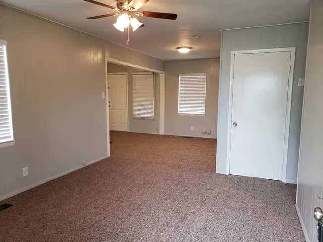 an empty room with chandelier fan and windows