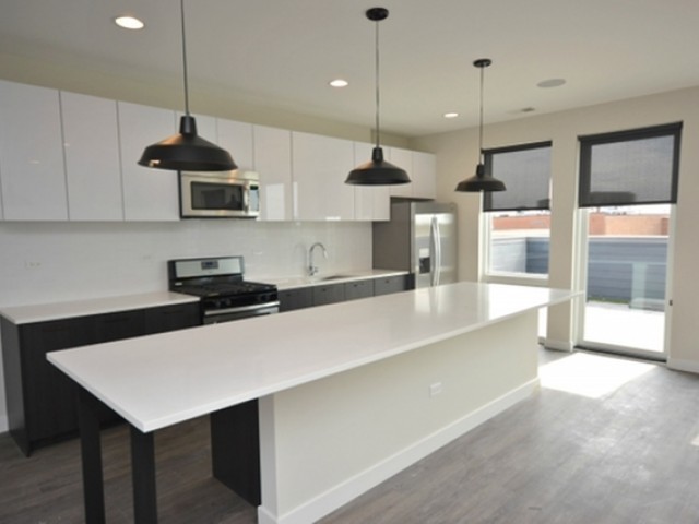 4027 North Broadway, Unit 504 Chicago, IL 60613 - Photo 3 of 7 a kitchen with stainless steel appliances a table a stove a refrigerator a sink and wooden floor