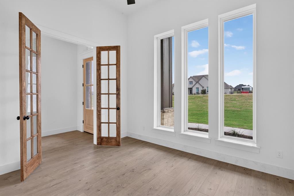 471 Red Bird Drive Springtown, TX 76082 - Photo 6 of 35 Room featuring three tall windows, light wood-finish flooring, white baseboards, and double French doors with black hardware