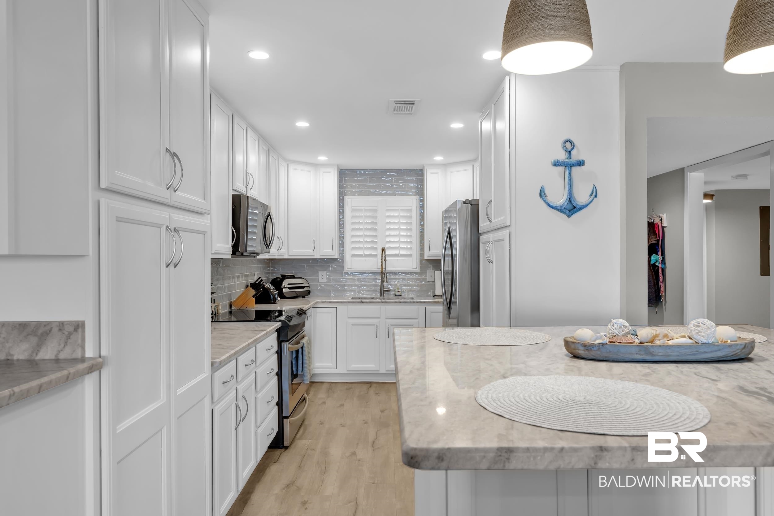 14100 River Road, Unit 211 Pensacola, FL 32507 - Photo 15 of 56 Kitchen featuring white shaker-style cabinetry, stainless steel appliances, light-toned wood-finish flooring, and a substantial island with a stone-finish countertop