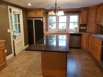 a kitchen with stainless steel appliances granite countertop a refrigerator a sink dishwasher a stove and a dining table with wooden cabinet