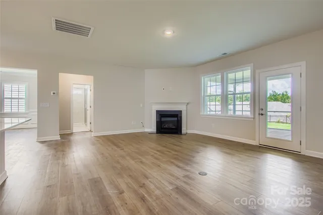 an empty room with wooden floor fireplace and windows