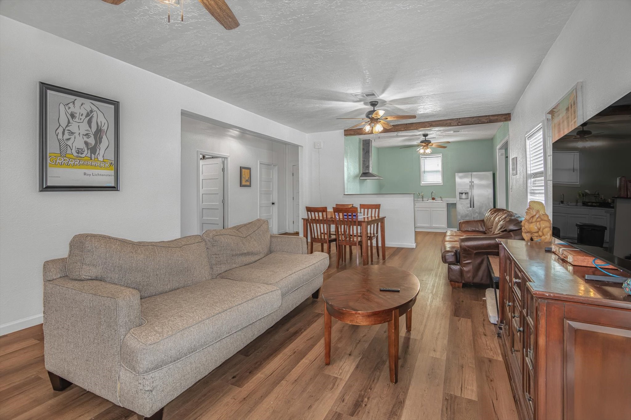905 43rd Street Galveston, TX 77550 - Photo 30 of 43 This inviting open-concept living space features a cozy living room with a plush sofa, a wooden dining set, and a modern kitchen. Warm wood flooring and ceiling fans enhance the comfort, while natural light brightens the area.