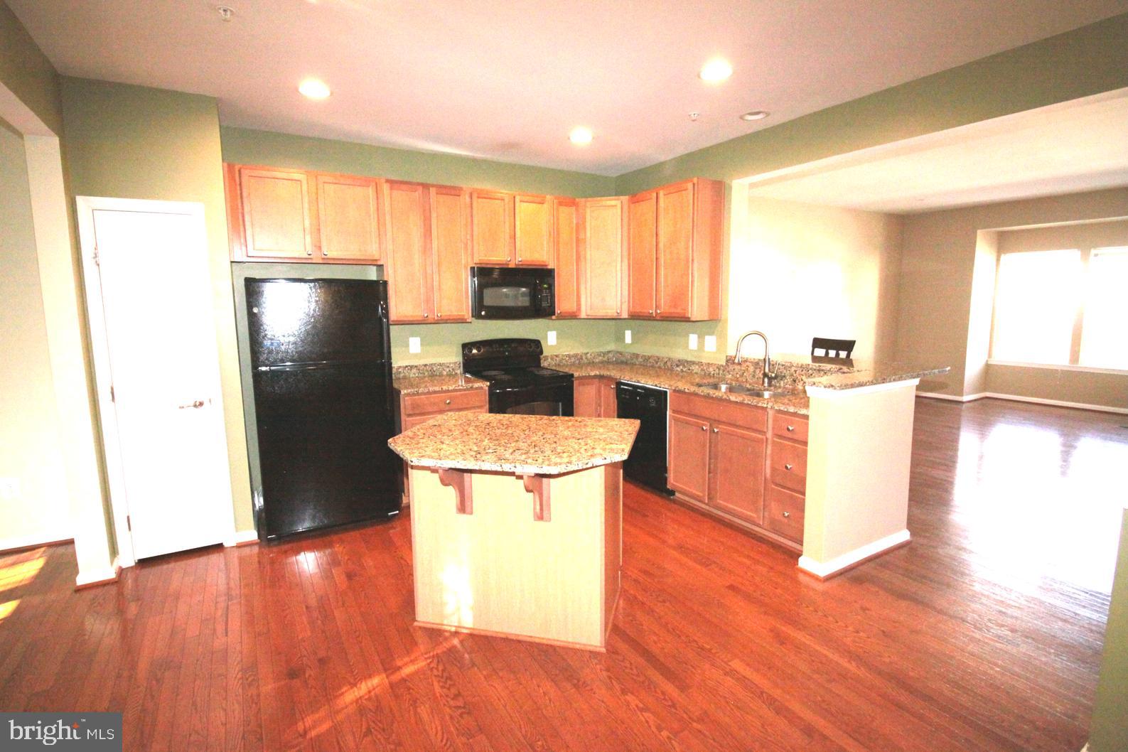 a kitchen with stainless steel appliances a refrigerator a sink a stove a microwave a center island and wooden floor