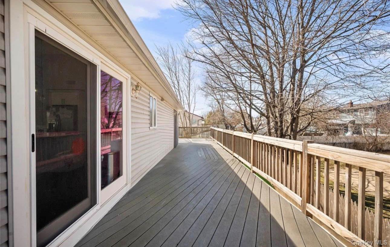 321 Sherbrooke Road Lindenhurst, NY 11757 - Photo 3 of 21 Spacious composite deck featuring composite decking with sturdy railings, sliding glass doors providing access to the interior, and mature tree backdrop offering natural screening and seasonal interest