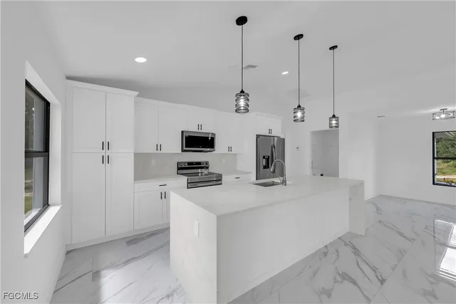 a view of a kitchen with stainless steel appliances kitchen island a sink dishwasher a refrigerator with white cabinets and wooden floor