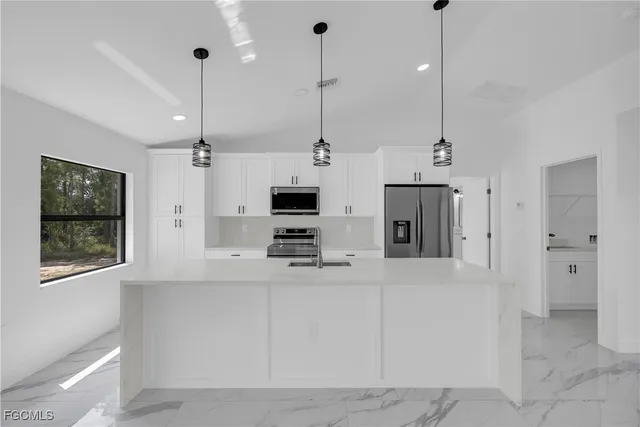 a kitchen with stainless steel appliances kitchen island granite countertop a refrigerator a sink and a chandelier