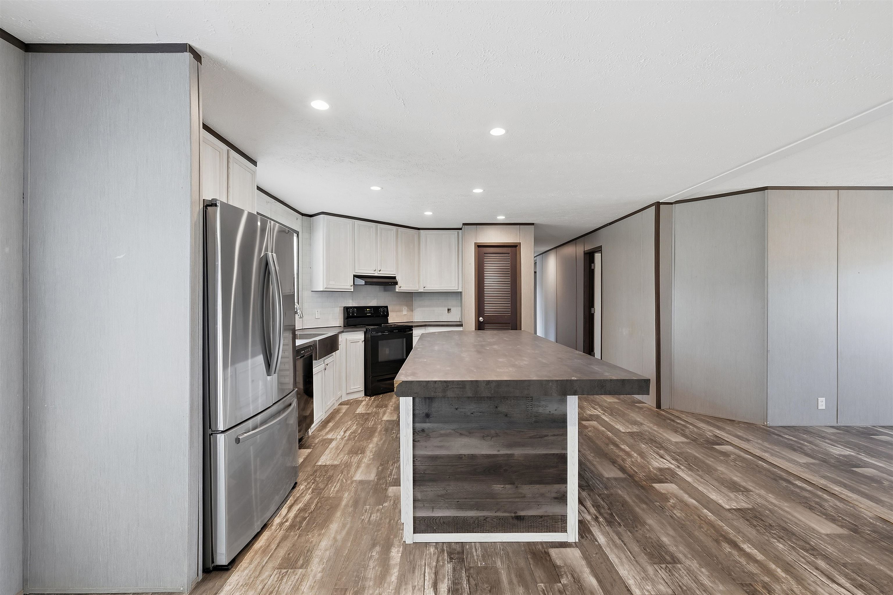 Kitchen featuring stainless steel appliances, black fixtures, light cabinetry, and an expansive island with wood-finish paneling
