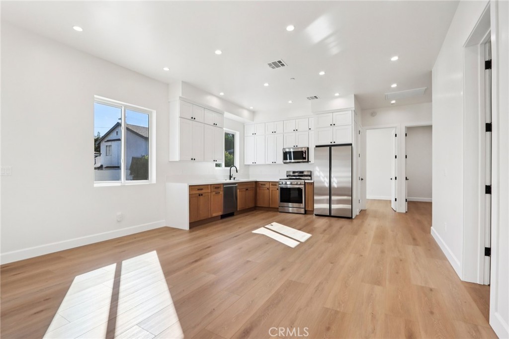 14931 Vose Street Van Nuys, CA 91405 - Photo 40 of 51 a large white kitchen with stainless steel appliances kitchen island a stove a refrigerator a sink dishwasher and a fireplace with wooden floor