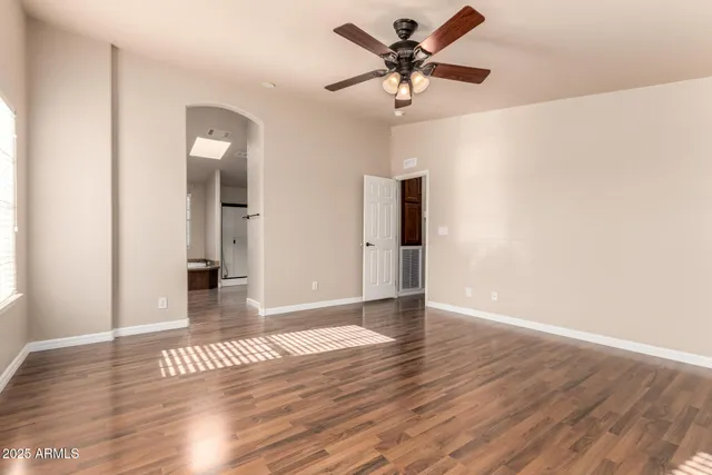 a view of an empty room with wooden floor and a ceiling fan
