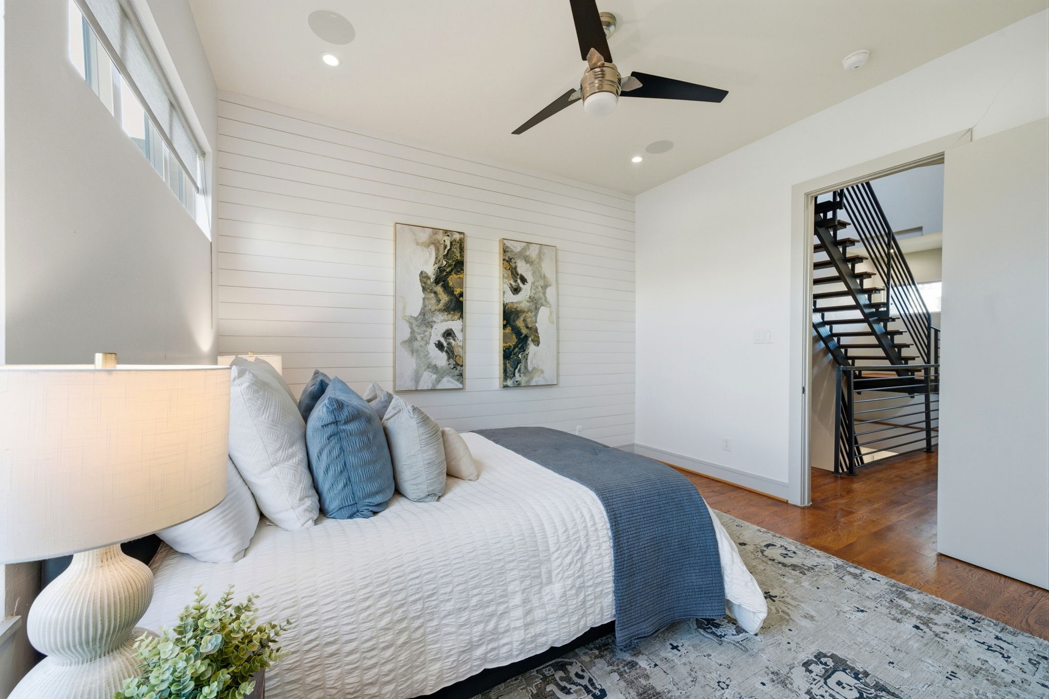 1405 Vermont Street, Unit A Houston, TX 77006 - Photo 34 of 46 Contemporary shiplap feature wall and polished hardwoods anchor this spacious first-floor guest suite. High ceilings and a modern ceiling fan enhance the airy atmosphere, while dual windows and recessed lighting ensure the room is bathed in light. This private retreat offers seamless access to the renovated ensuite bath and is positioned near the home's striking floating staircase.